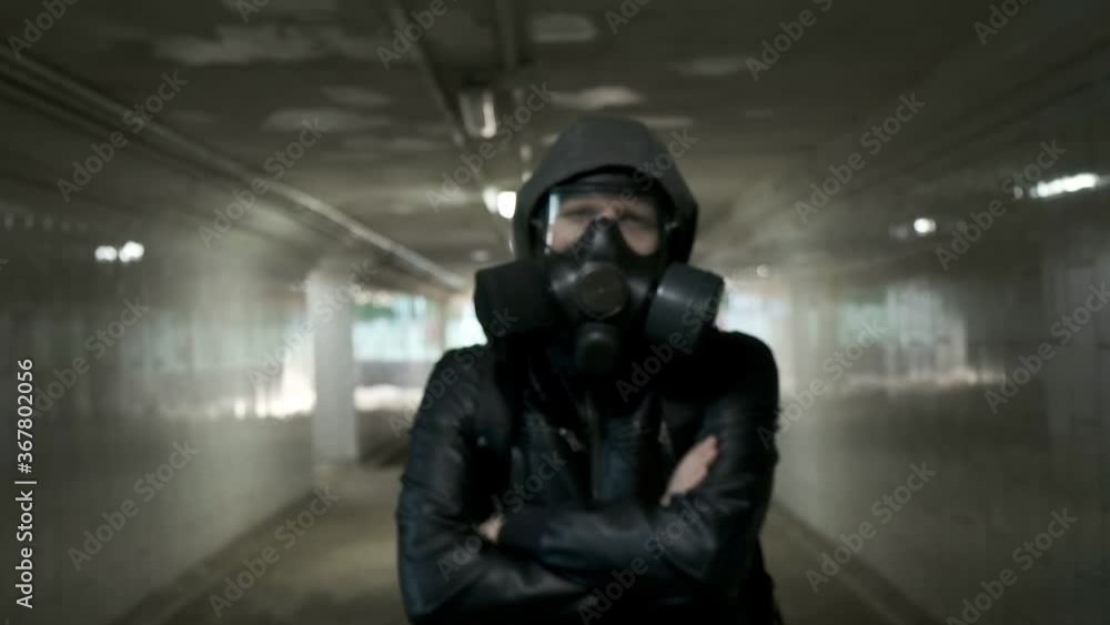 man in gas mask, black jacket with hood standing in long tunnel, underpass. protection from chemical weapons, virus epidemic. Post apocalyptic world. survivor, stalker after nuclear war. slow motion man in gas mask, black jacket with hood standing in long tunnel, underpass. protection from chemical weapons, virus epidemic. Post apocalyptic world. survivor, stalker after nuclear war. slow motion