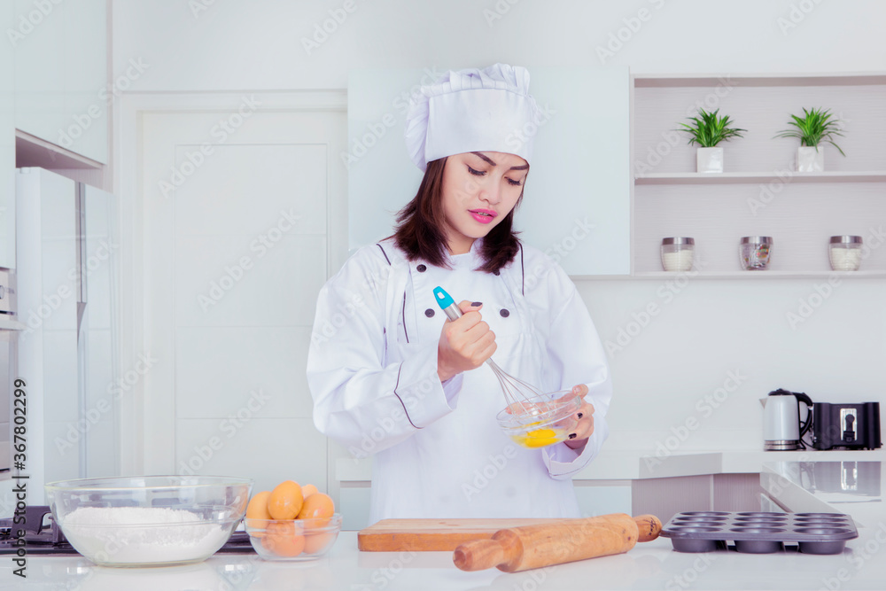 Female baker whisking eggs in a bowl to make cakes Female baker whisking eggs in a bowl to make cakes