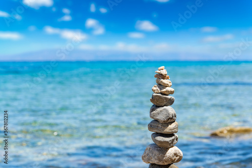 Closeup of Cairn of pebbles, Zen stack of stones on the sea stone beach under blue sky during sunny day in Greece