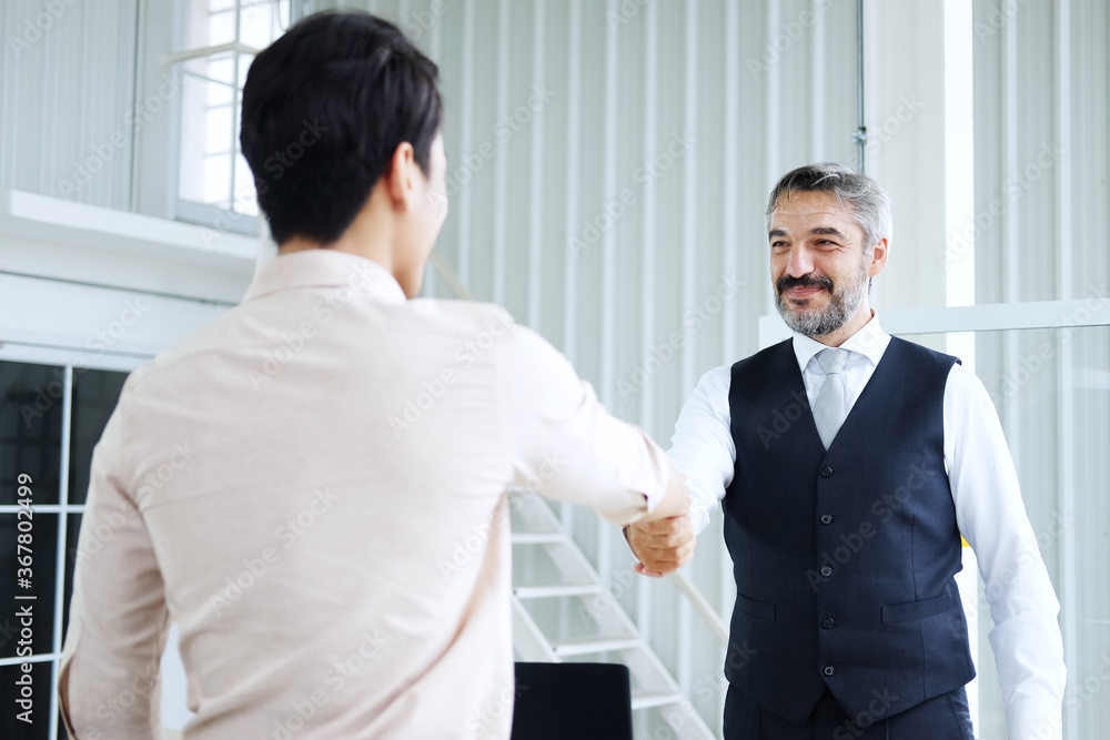 Smiling Senior Caucasian manager shaking hand with young Asain businessman after meeting and successful corporate in project Smiling Senior Caucasian manager shaking hand with young Asain businessman after meeting and successful corporate in project