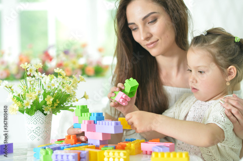 Little daughter and happy mother playing with colorful plastic blocks