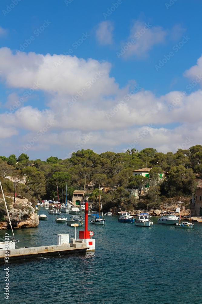 View of the Bay of Cala Figuera with many yachts against a blue sky with clouds.
