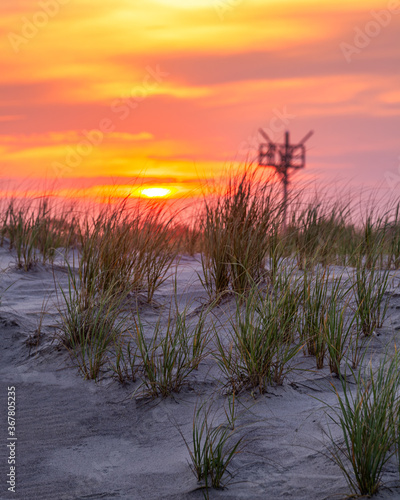 Fototapeta Naklejka Na Ścianę i Meble -  Sand dunes with a vibrant sunset in the background. Selective focus on the beach grass and dune in the foreground. Copy space in the sky