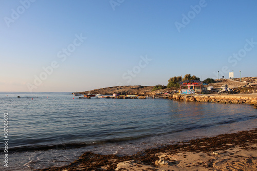 Sandy city beach with seaweed of Ayia NAPA against the blue sky.