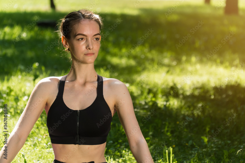 stylish young girl in sports fitness clothes, against the backdrop of a green park on a fresh cheer
