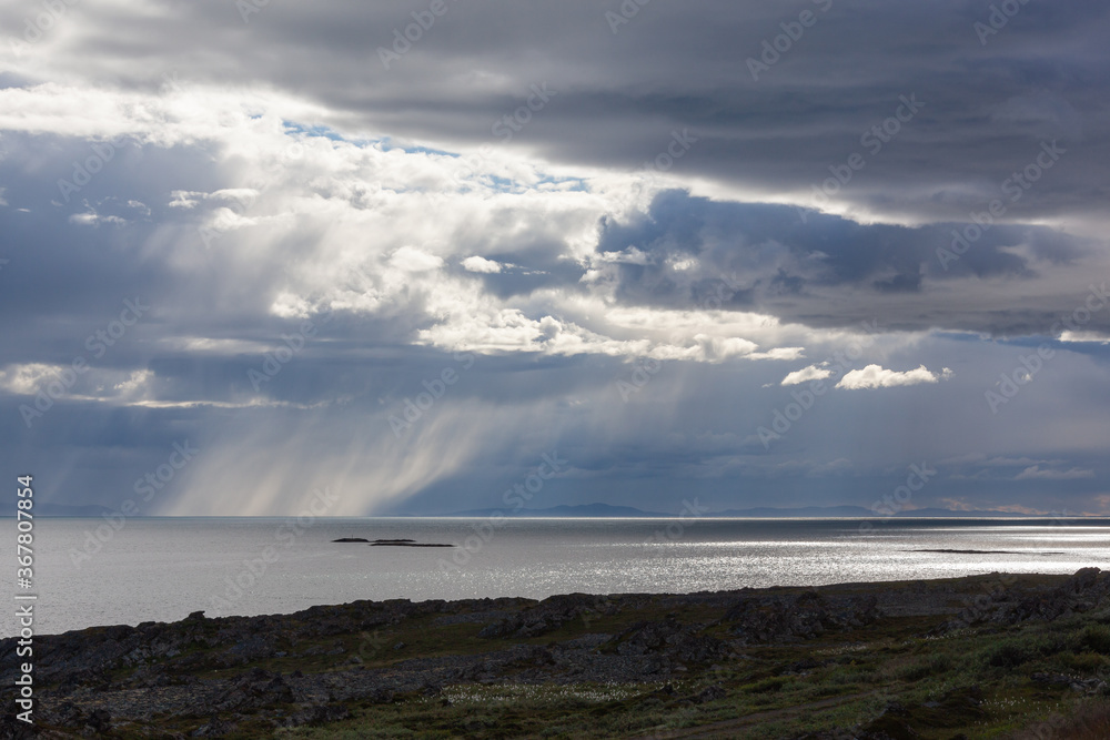 Thunderclouds lit with sunshine with the rain over Barents sea, Finnmark, Norway