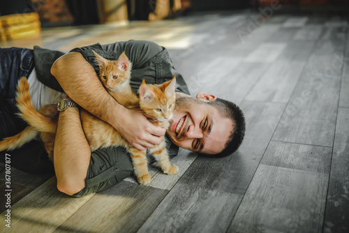 Photography a young guy lies on the floor and hugs maine coon cats