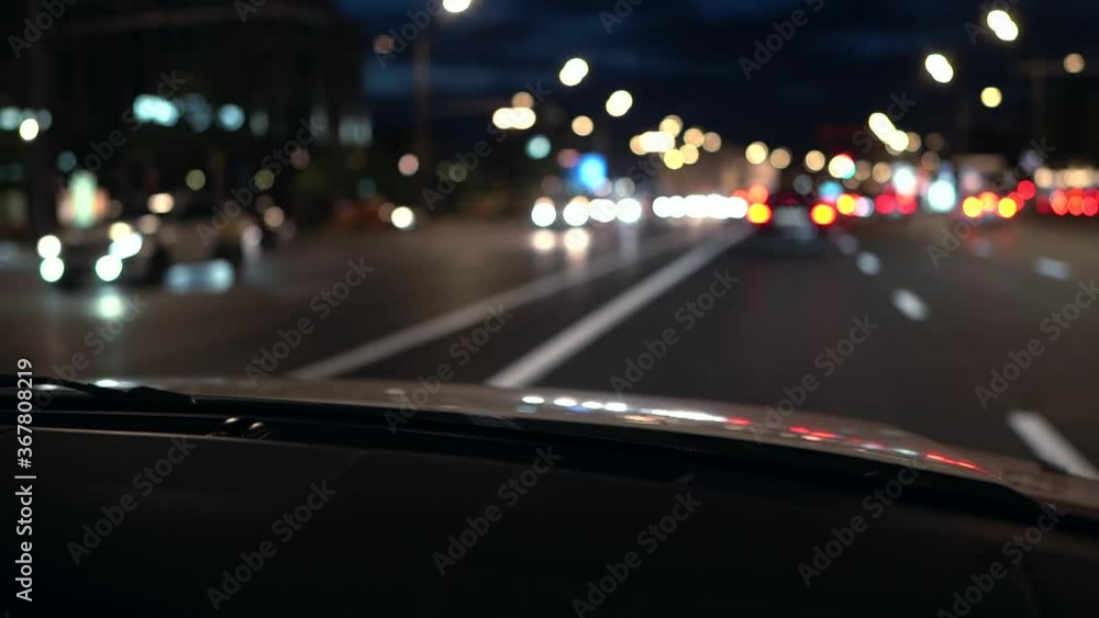 The blurred movement of the side on the road at night. Round colorful bokeh shines from car headlights in traffic through the hood of the car. The blurred movement of the side on the road at night. Round colorful bokeh shines from car headlights in traffic through the hood of the car.