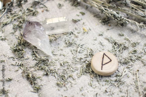 Scandinavian wooden rune Wunjo on a rough linen cloth with amethyst crystalline, rock crystal and dried wormwood