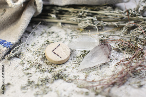 Scandinavian wooden rune Kauna, Kenaz on a rough linen cloth with amethyst crystalline, rock crystal and dried wormwood
