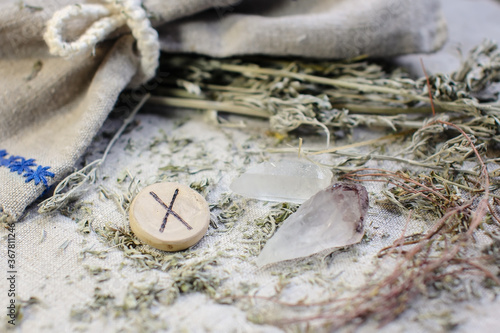 Scandinavian wooden rune Gebu, Gyfu on a rough linen cloth with amethyst crystalline, rock crystal and dried wormwood photo