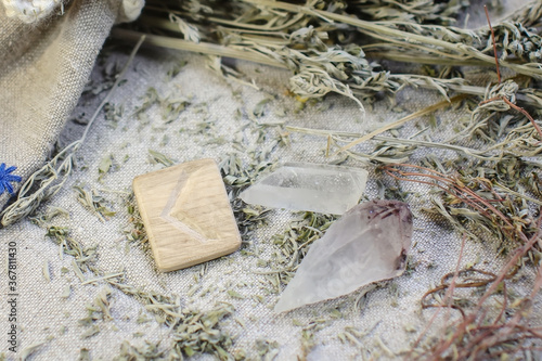 Scandinavian wooden rune Kauna, Kenaz on a rough linen cloth with amethyst crystalline, rock crystal and dried wormwood