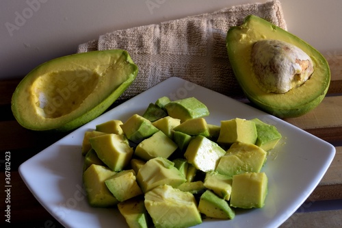 Closeup shot of cut-up pieces of avocado pieces on a plate and halved avocados on a kitchen table photo