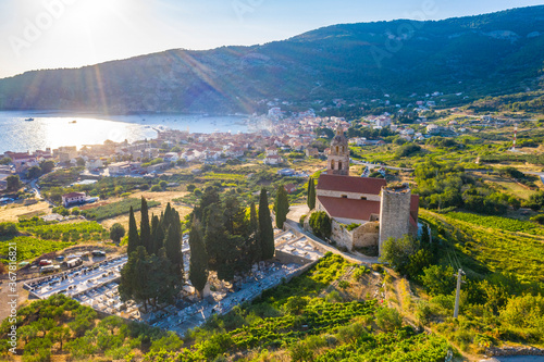 Aerial panoramic view of the cathedral St.Nicholas in Komiza city - the one of numerous port towns in Croatia  orange roofs of houses  picturisque bay  mountain is on background