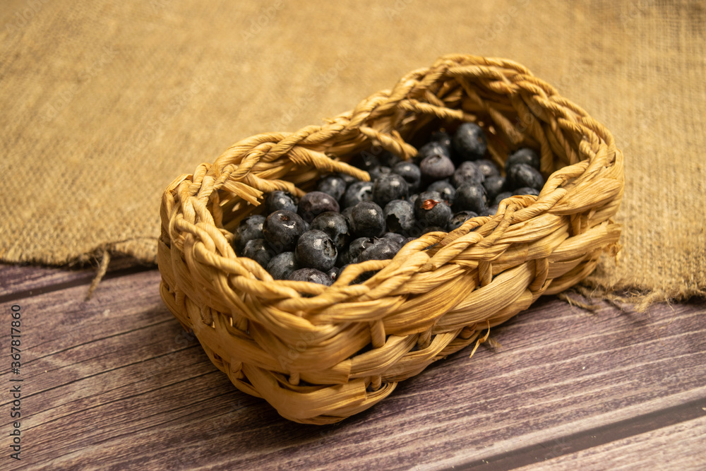 Blueberry in a wicker basket on a background of homespun fabric with a rough texture. Close up. Blueberry in a wicker basket on a background of homespun fabric with a rough texture. Close up.