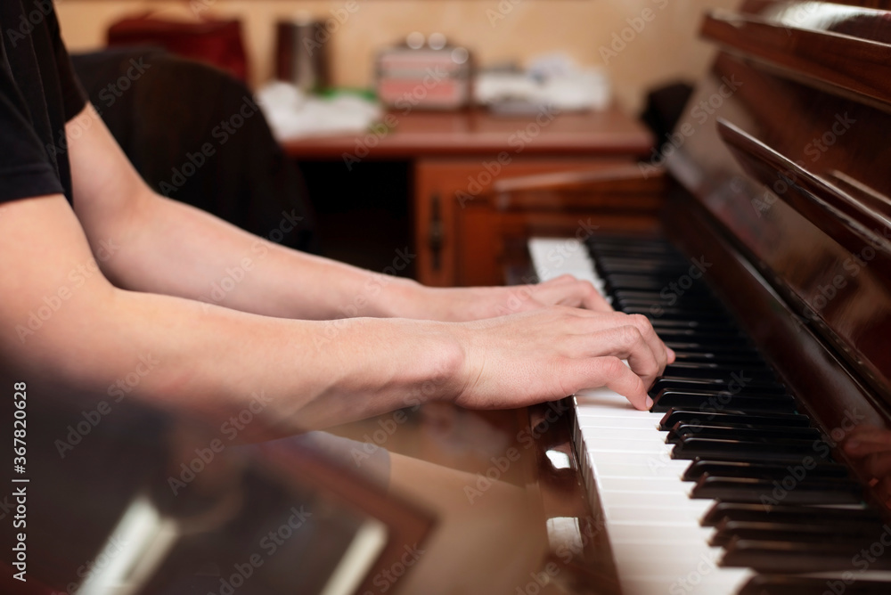 Fototapeta premium Hands of a young boy on the piano keys, a teenager plays a melody from a famous movie, he is engaged in music for self-development