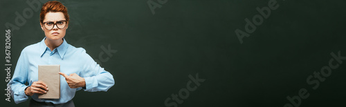 Foto horizontal image of strict teacher in eyeglasses pointing at book while standing
