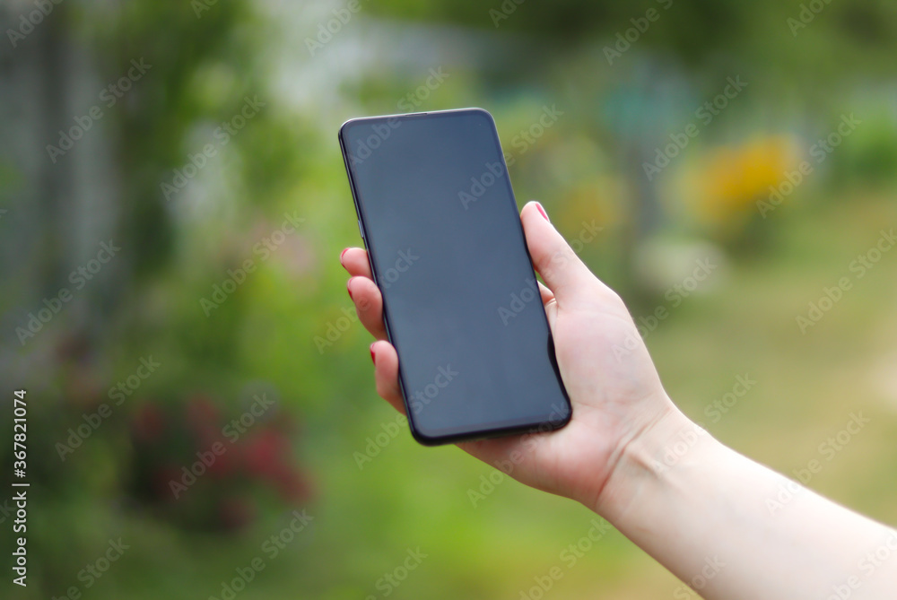 Mobile phone in a female hand with red manicure. Blurred green bokeh background.