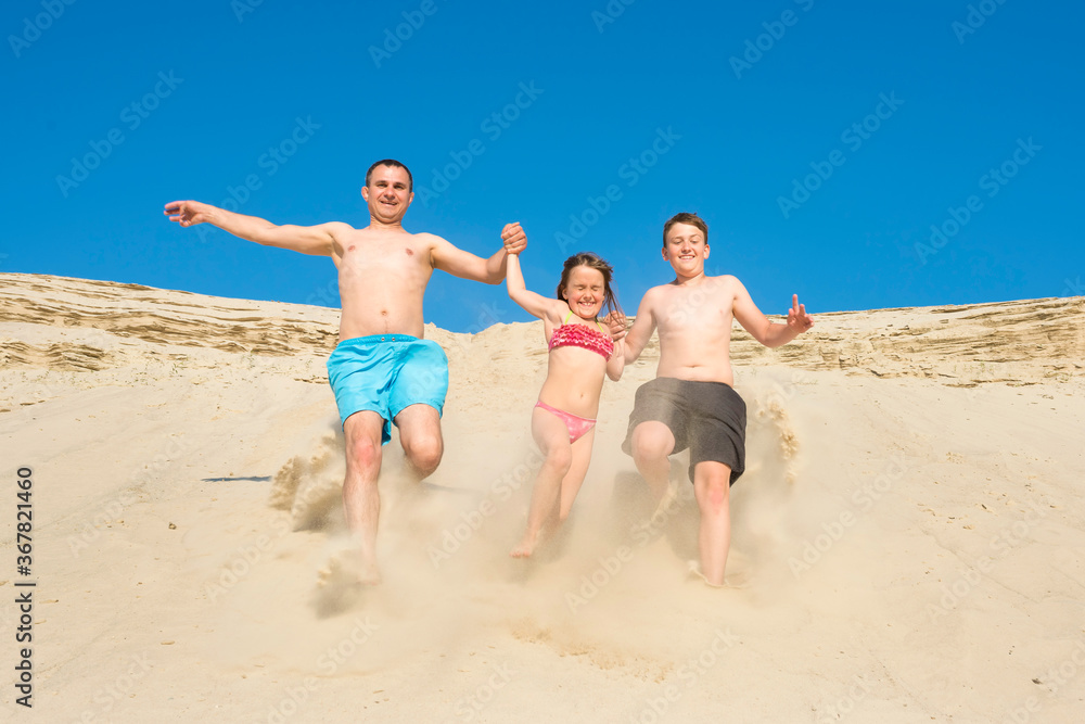 Family running on the beach sand on a sunny summer day. Family games on vacation. Sports and active lifestyle concept.