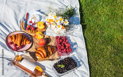 Summertime eco picnic setting on the grass with croissant, peaches, berries and wine on white tablecloth.