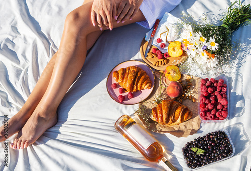 Summertime eco picnic setting on the grass with croissant, peaches, berries and wine on white tablecloth. Top