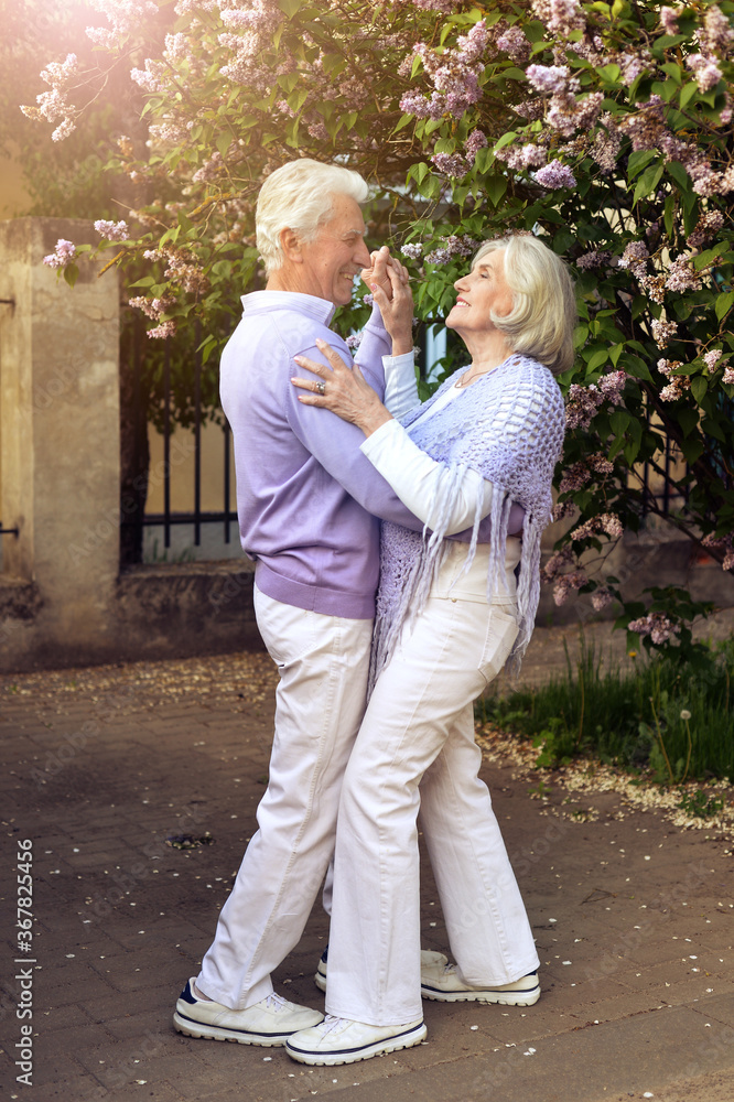 Beautiful senior couple dancing in the park by lilacs