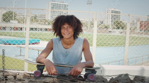 Hispanic latin young man holding skateboard and smiling, portrait of happy skater in skatepark spain, barcelona, brazilian male professional skateboarder photo