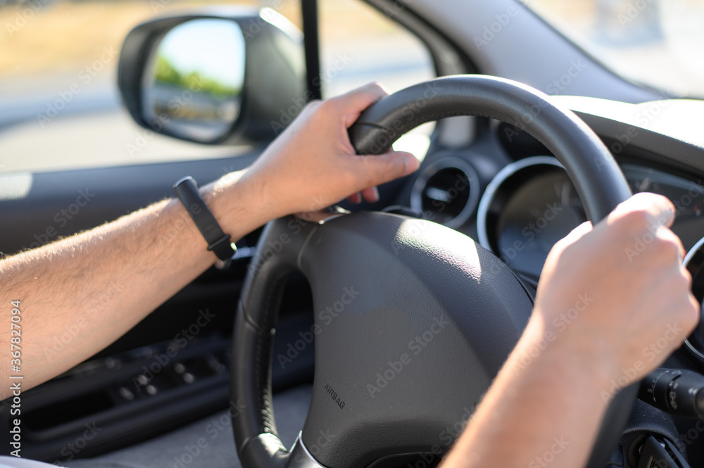 The man is driving. Men's hands hold the steering wheel of the car. Selective focus.