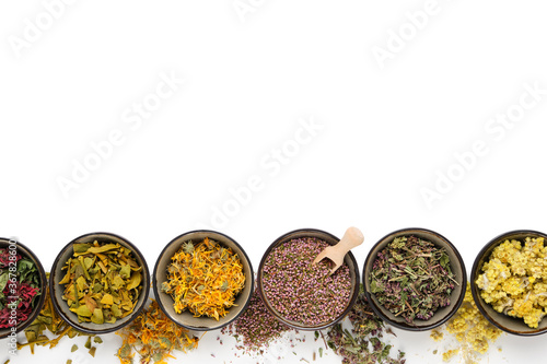 Black bowls of dry medicinal herbs on white background. Top view, flat lay. Alternative medicine. Copy space for text. photo