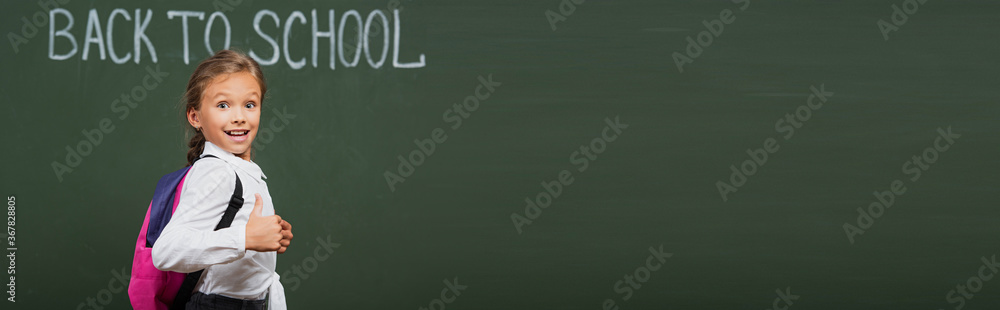 horizontal concept of happy schoolgirl with backpack near chalkboard with back to school inscription