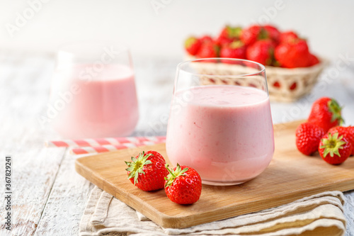 Glass with strawberry smoothie or milkshake on wooden table. Summer drink.