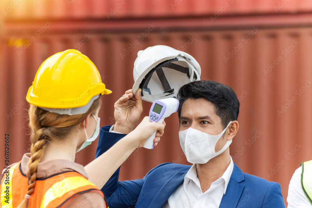 industrial worker woman temperature checking fever by digital thermometer with businessman with cargo container in background at container cargo harbor, industrial, logistic import and export concept industrial worker woman temperature checking fever by digital thermometer with businessman with cargo container in background at container cargo harbor, industrial, logistic import and export concept