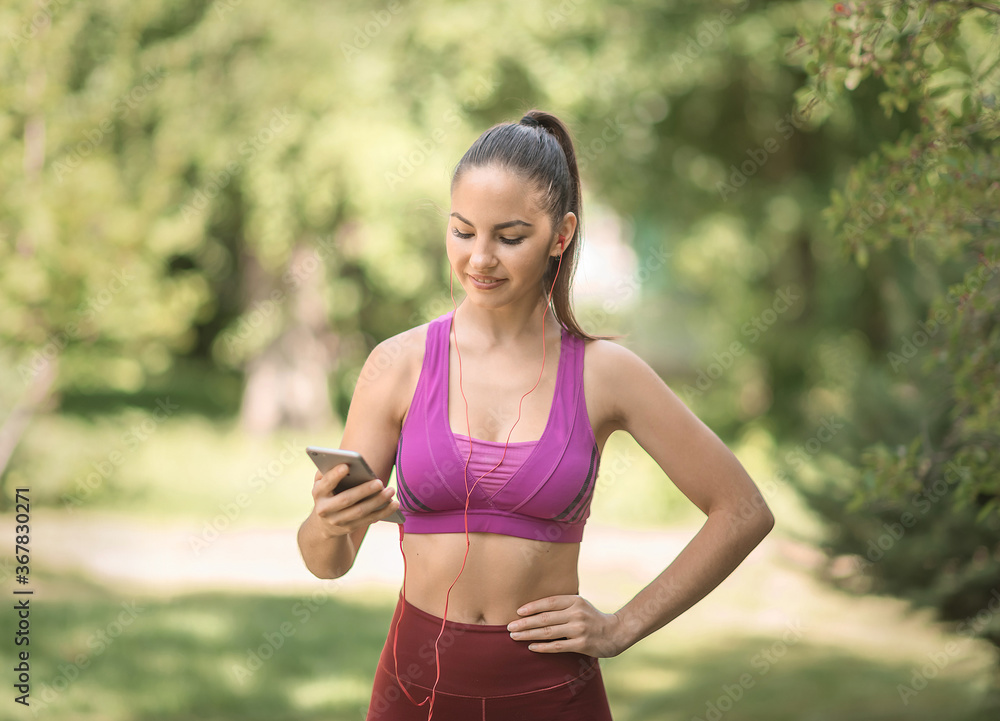 Girl athlete in a red uniform smiling in the park with a phone and headphones. Stands right up close. Girl athlete in a red uniform smiling in the park with a phone and headphones. Stands right up close.
