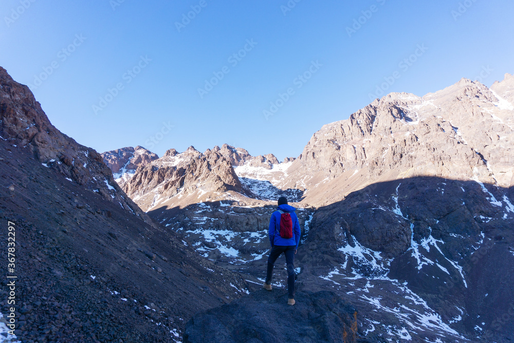 A man looking at the beautiful panorama of  mountain peaks and blue sky, after hiking to the Toubkal mountain in Morocco