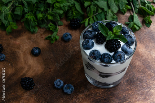 Cottage cheese dessert with blueberries, blackberries and mint in a transparent glass glass. On a wooden background. Yummy.