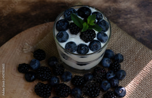 Cottage cheese dessert with blueberries, blackberries and mint in a transparent glass glass. On a burlap napkin and on a wooden background. Delishious. photo