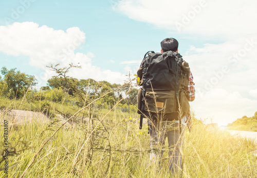 A man with backpack walking in the green field while traveling