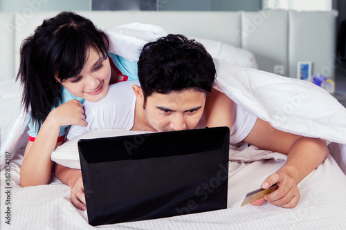 Young couple lying on bed while shopping online