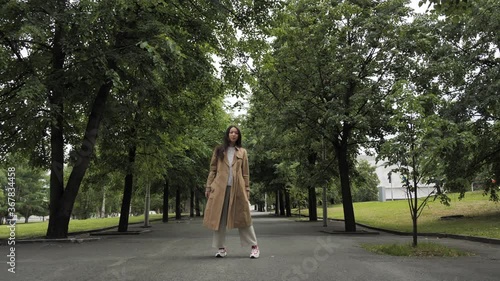 A young woman poses for a camera in a park among the trees in the summer. Walk in the park. High quality 4k footage