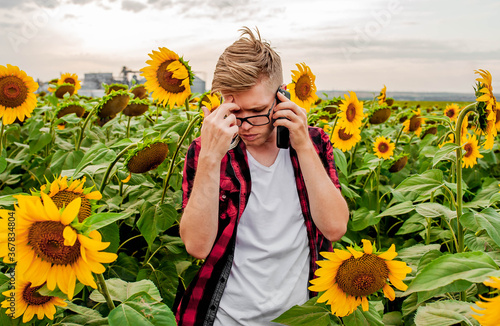 The guy is talking by mobile phone  in a field with sunflowers. Agriculture manager concept