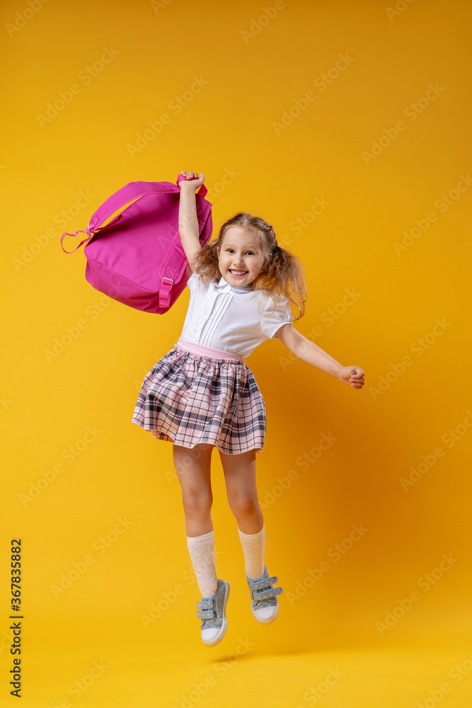 mischievous schoolgirl in uniform with backpack jumps on yellow background