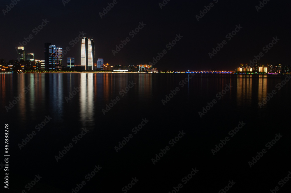 Suzhou business center viewed from the lake with colorful lights reflecting in the water.