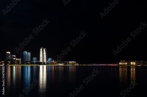 Suzhou business center viewed from the lake with colorful lights reflecting in the water.