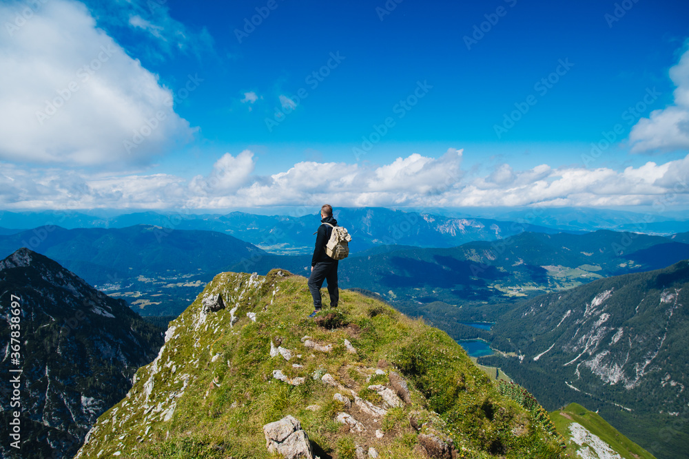 A tourist stands on top of a mountain with a backpack and looks into the distance. Trekking in the mountains.