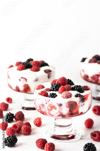 Delicious juicy berries of raspberries and blackberries with yoghurt in a glass form on a white background