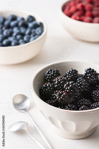 Raspberries, blueberries and blackberries close-up in bowls on a white background, ripe juicy berries