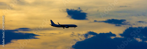 Airplane taking off at the sunset sky, silhouette of aircraft in the sky. Wide banner background