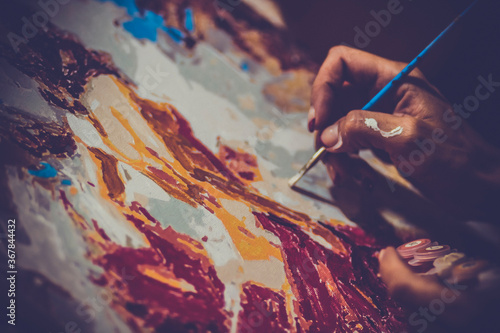 Brush in the hand of an artist drawing a picture on the canvas
