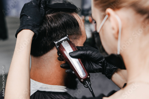 Woman barber cutting hair to a bearded man in face mask. Quarantine haircut concept.