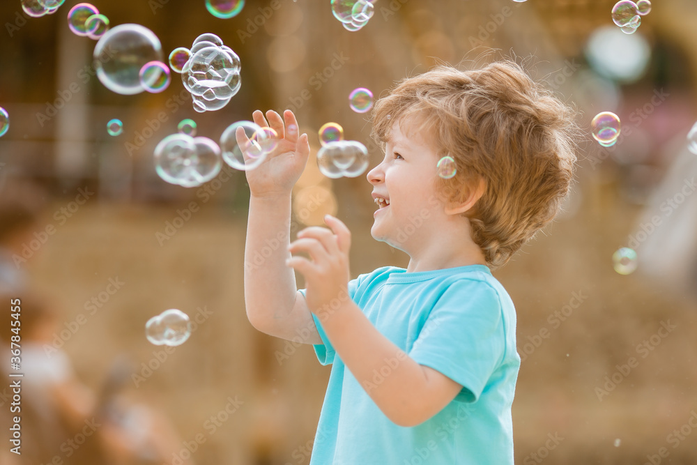 Happy baby boy plays with soap bubbles in a summer amusement park. Children's Lifestyle